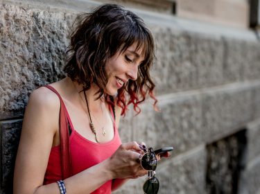 Frau in rotem Top schaut auf ihr Smartphone.