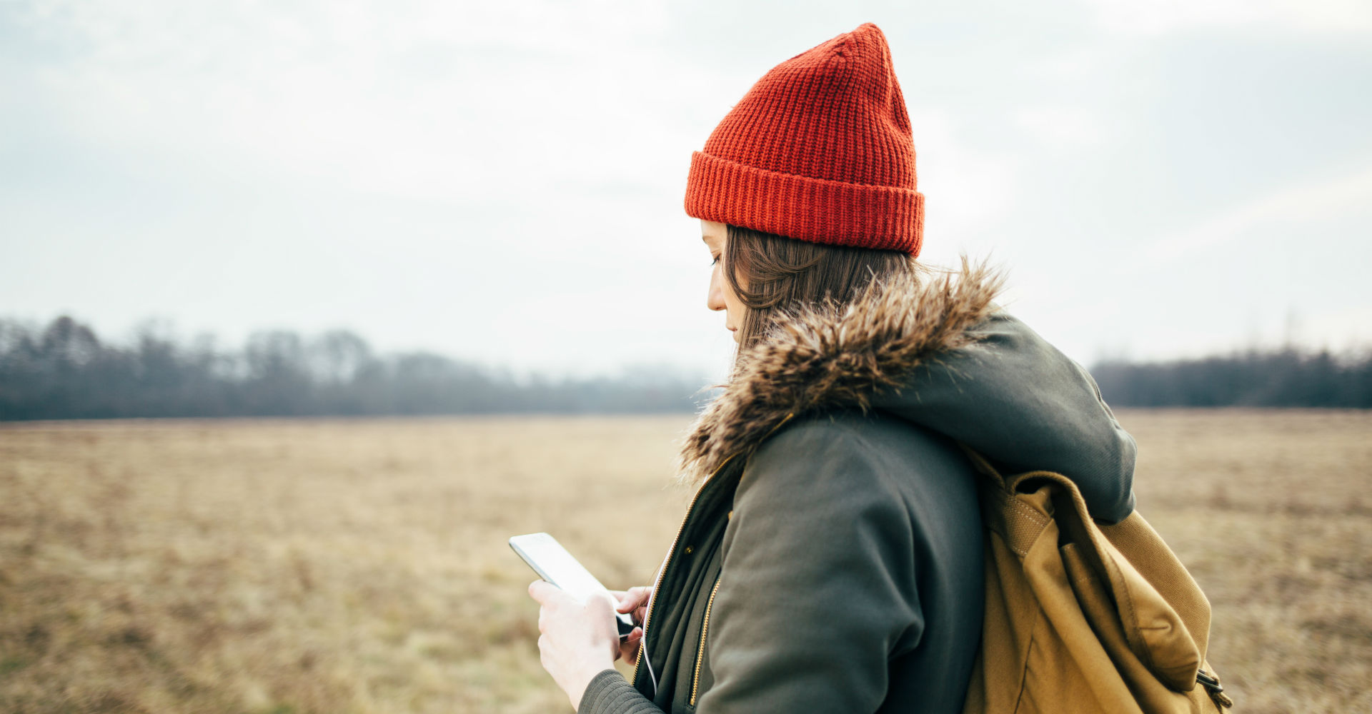 Junge Frau ist draußen unterwegs und schaut auf ihr Smartphone.