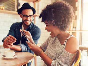 Lachende Frau mit Smartphone im Cafe