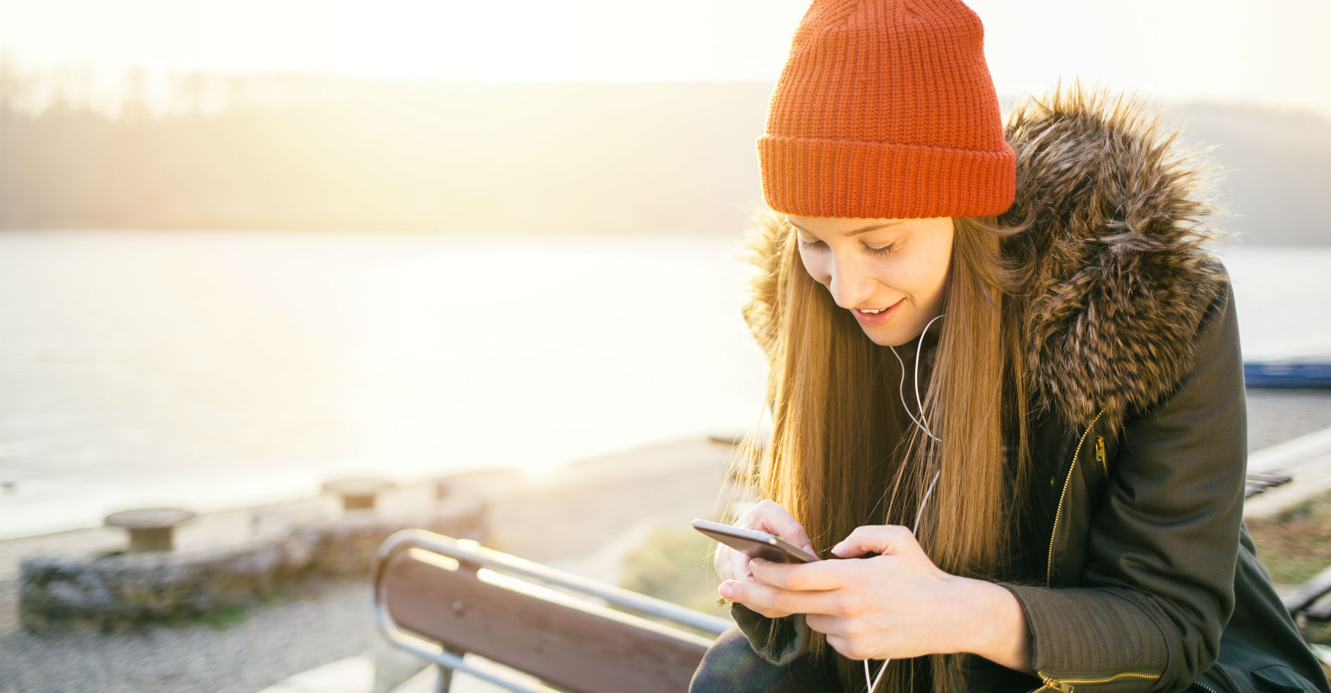 Junge Frau in grünem Parka schaut auf ihr Smartphone.