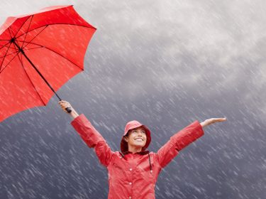 Frau mit Regenschirm lacht über den Regen