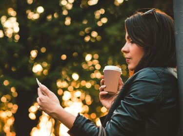 Junge Frau checkt draußen Mails an ihrem Smartphone.