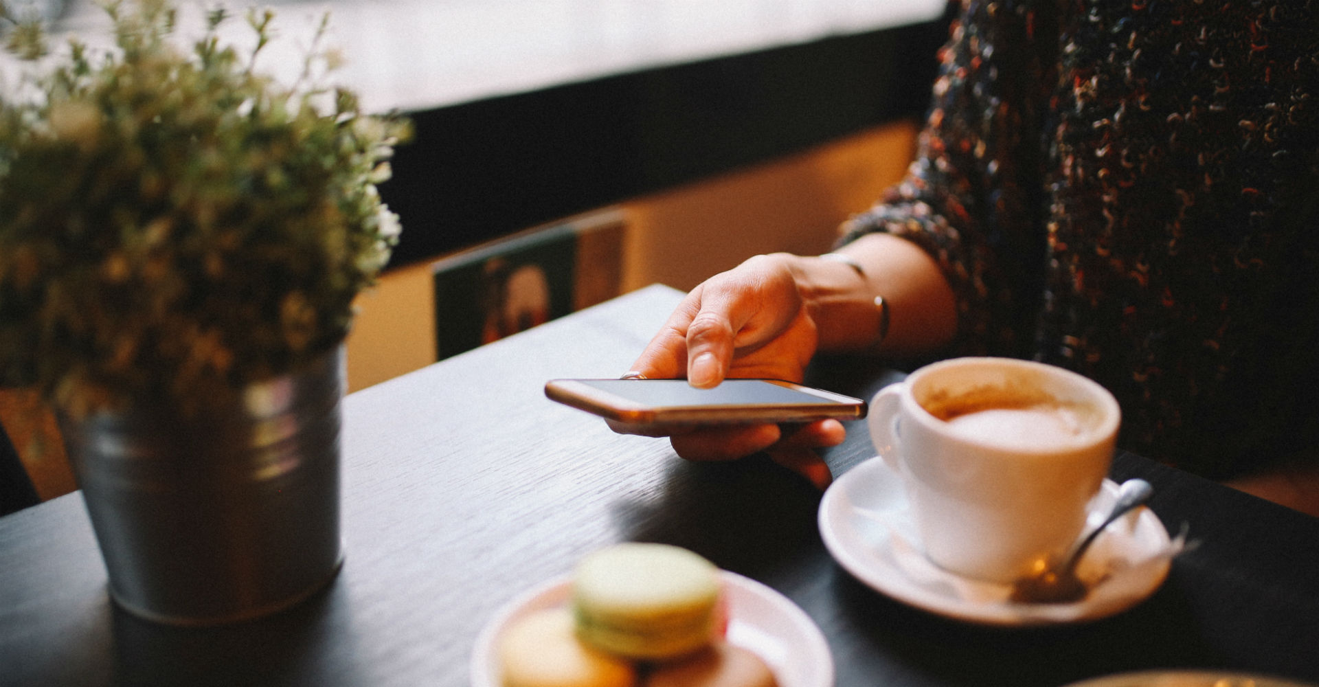 Junge Frau öffnet die Alexa-App auf dem Smartphone am Frühstückstisch.