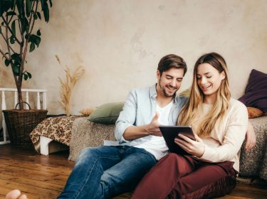 Junges Paar spielt mit dem Tablet im Wohnzimmer.