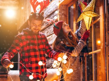 Junges Paar hängt leuchtende Weihnachtsdekoration auf