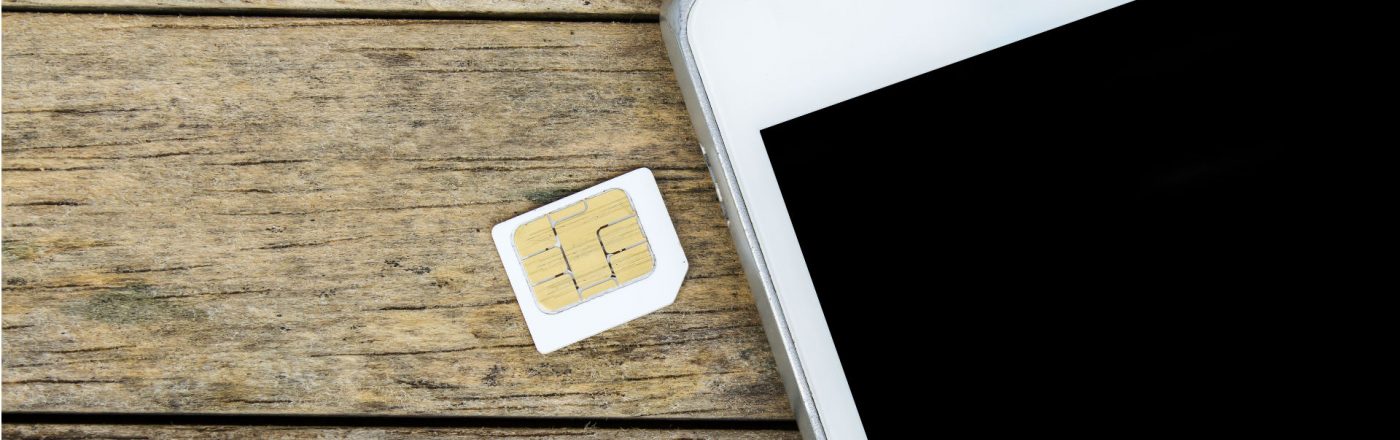 SIM-Karte liegt neben einem weißen Smartphone auf einem Holztisch.