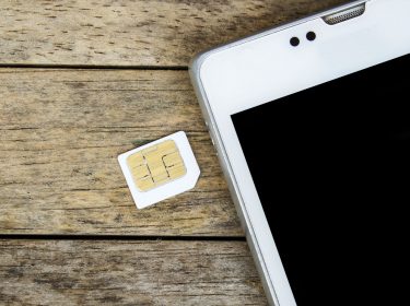 SIM-Karte liegt neben einem weißen Smartphone auf einem Holztisch.