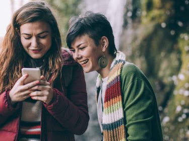 Zwei Freundinnen schauen lachend auf ein Smartphone.