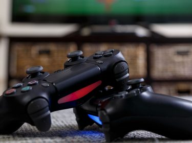 Zwei PS4-Controller liegen auf dem Teppich vor dem Fernseher.