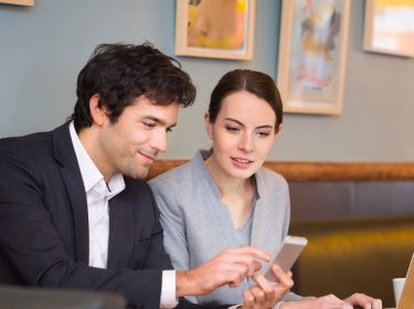 Ein Mann nutzt via Smartphone den Hotspot einer Frau auf dem Laptop