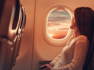 Eine Frau sitzt im Flugzeug und schaut entspannt aus dem Fenster