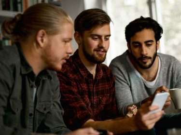 Drei junge Gamer chatten über das Smartphone mit ihrem Freunden.