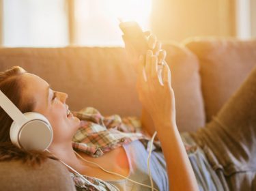 Junge Frau hört ein Hörbuch via Smartphone auf dem Sofa