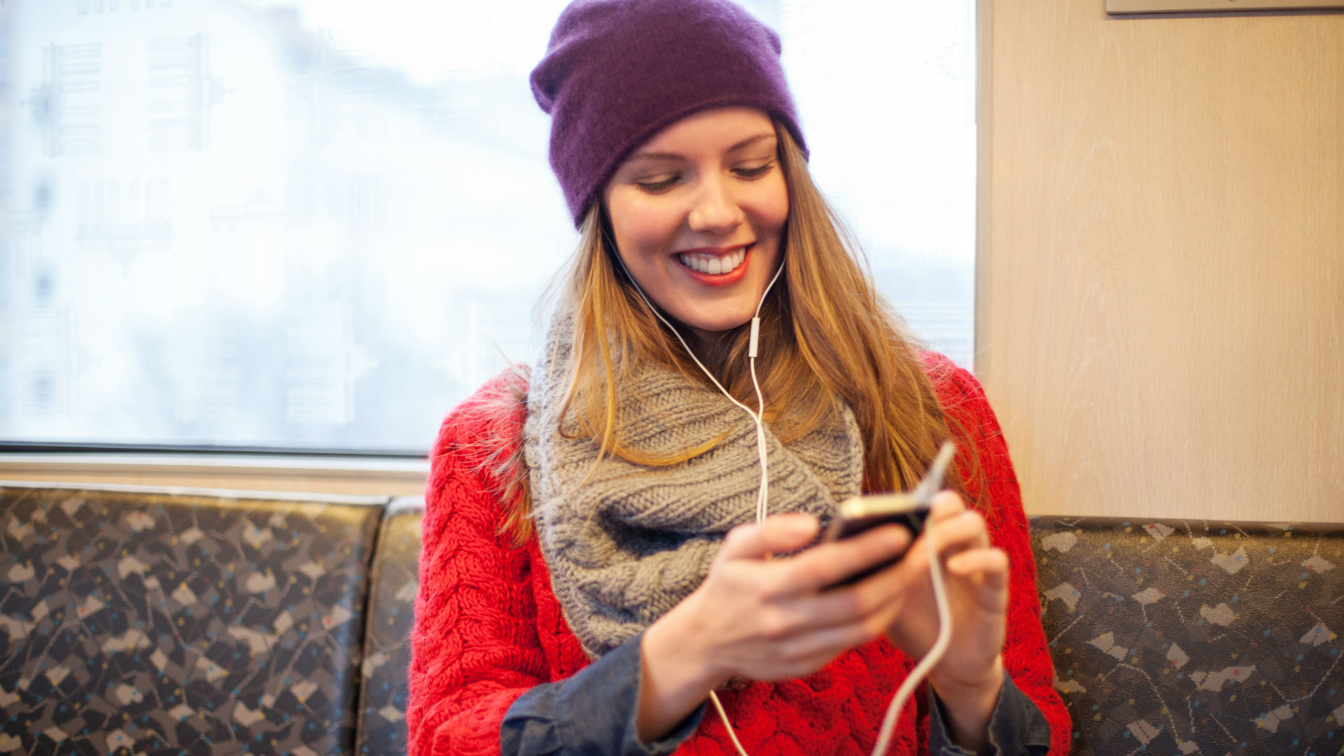 Junge Frau sitzt in der Bahn und nutzt Gehirnjogging-Apps am Smartphone.