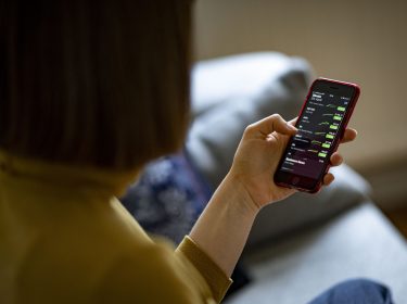 Frau hält iPhone in der Hand und checkt Aktienkurse