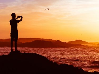 Junger Mann macht mit seinem Smartphone ein Foto vom Sonnenuntergang.