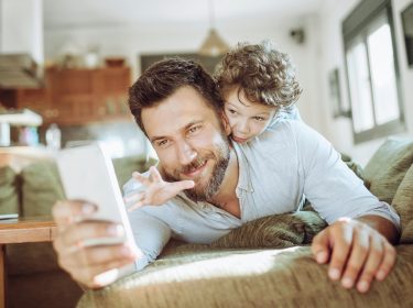 Ein junger Vater spielt mit seinem Sohn und hält ein Smartphone