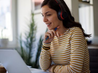 Eine junge Frau arbeitet an einem Laptop und nutzt ein kabelloses Headset