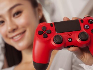 Frau hält einen roten PS4-Controller in die Höhe.