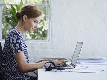 Junge Frau sitzt am Schreibtisch und arbeitet am Laptop