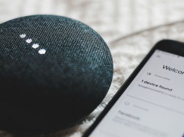 Schwarzer Google Home Mini liegt neben Smartphone.