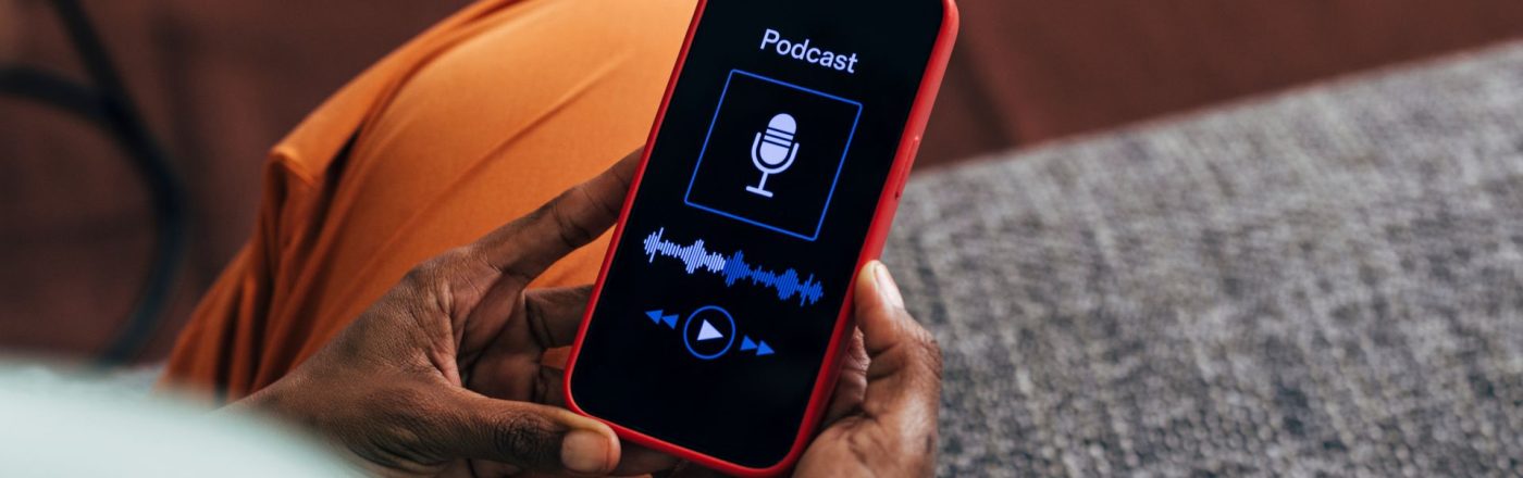 Person Holding Red Smartphone Displaying Podcast Screen Indoors