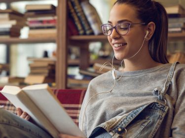 Eine junge Frau hört ein Hörbuch und liest zeitgleich