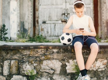 Ein Junge sitzt auf der Mauer und beschäftigt sich mit Facebook