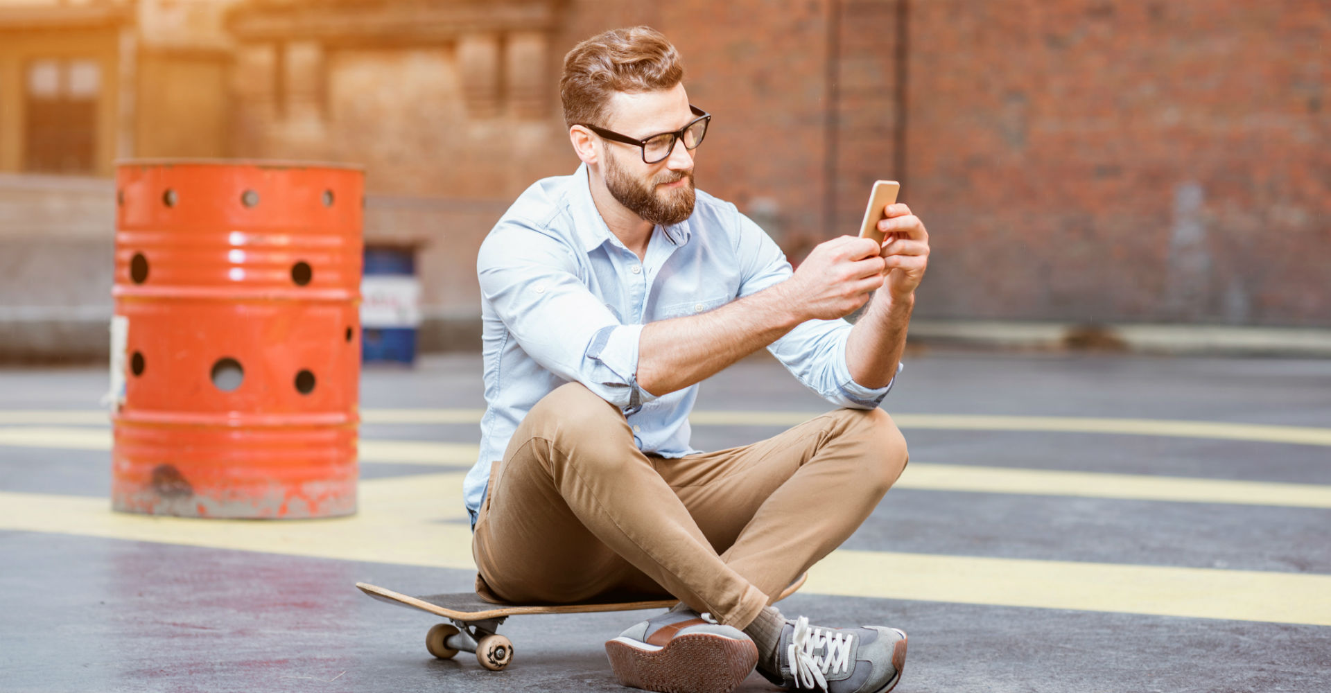 Junger Mann sitzt auf dem Skateboard und nutzt sein Smartphone.