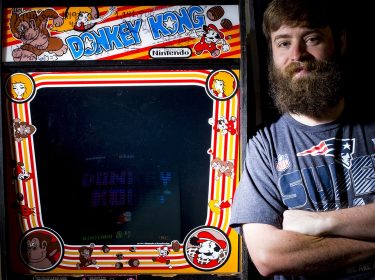 Ein Mann steht neben einem Donkey Kong Arcade-Spielautomaten