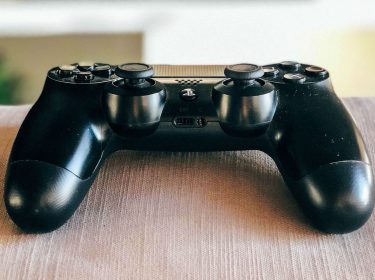 Schwarzer PS4-Controller liegt auf der Couch.