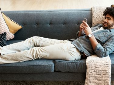 Junger Mann sitzt entspannt auf dem Sofa.