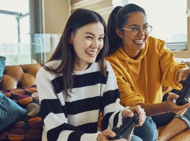 Zwei Freundinnen zocken mit ihren Controllern ein PS4-Spiel.