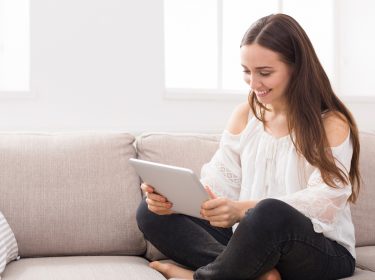 Junge Frau sitzt mit Tablet auf der Couch