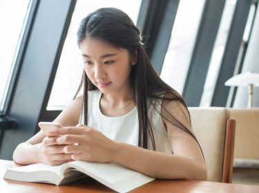 Eine junge Frau lernt mit ihrem Smartphone in der Bibliothek und nutzt dabei den Google Assistant