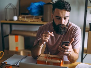 Junger Mann sitzt mit Smartphone an seinem Schreibtisch
