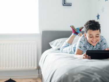 Ein Kind liegt auf dem Bett und spielt mit seinem Tablet