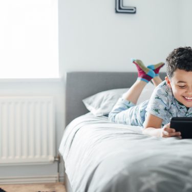 Tablets für Kinder Ein Kind liegt auf dem Bett und spielt mit seinem Tablet