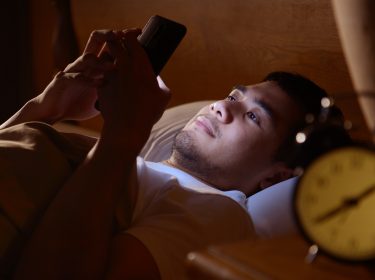 Mann mit Smartphone und Wecker