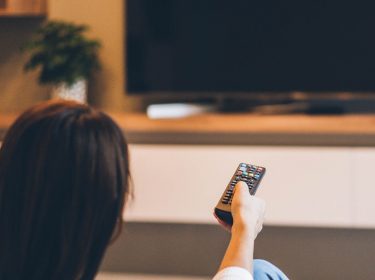 Junge Frau schaltet am TV die Audiodeskription von Netflix ein.