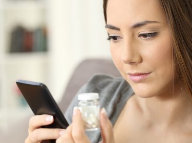 Eine Frau betrachtet Tabletten und ein Smartphone.