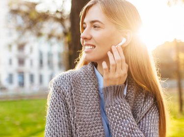 Junge Frau hört Musik von Deezer mit ihren Bluetooth-Kopfhörern.