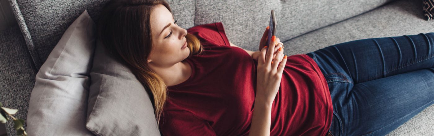 Android 10: Diese Geräte sollen das Update erhalten Junge Frau lädt Android 10 auf ihr Gerät, während sie auf dem Sofa liegt.