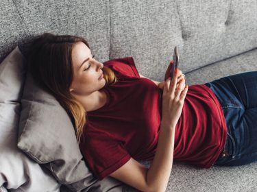 Junge Frau lädt Android 10 auf ihr Gerät, während sie auf dem Sofa liegt.