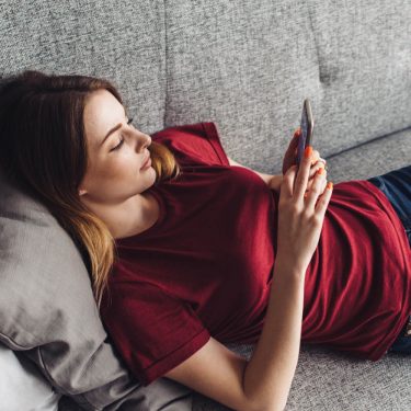 Android 10: Diese Geräte sollen das Update erhalten Junge Frau lädt Android 10 auf ihr Gerät, während sie auf dem Sofa liegt.