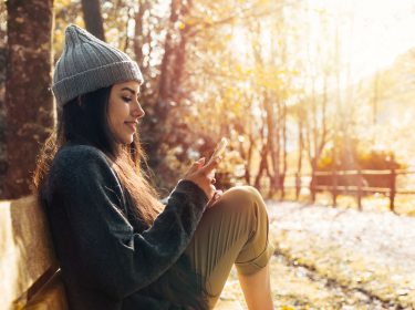 Frau sitzt im Park und schaut auf ihr iPhone.