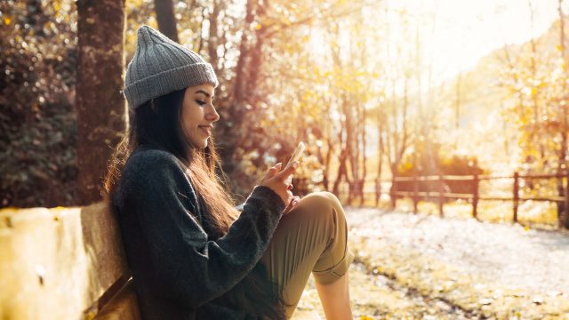 Frau sitzt im Park und schaut auf ihr iPhone.