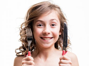 Kleines Mädchen mit Messer und Gabel