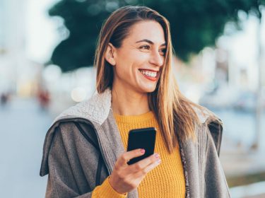 Frau hält Smartphone in der Hand, auf dem sie Harry Potter:Wizards Unite spielt.