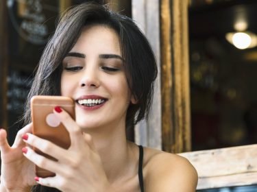 Frau schaut auf ihr Smartphone und entdeckt eine neue Google-Assistant-Funktion.